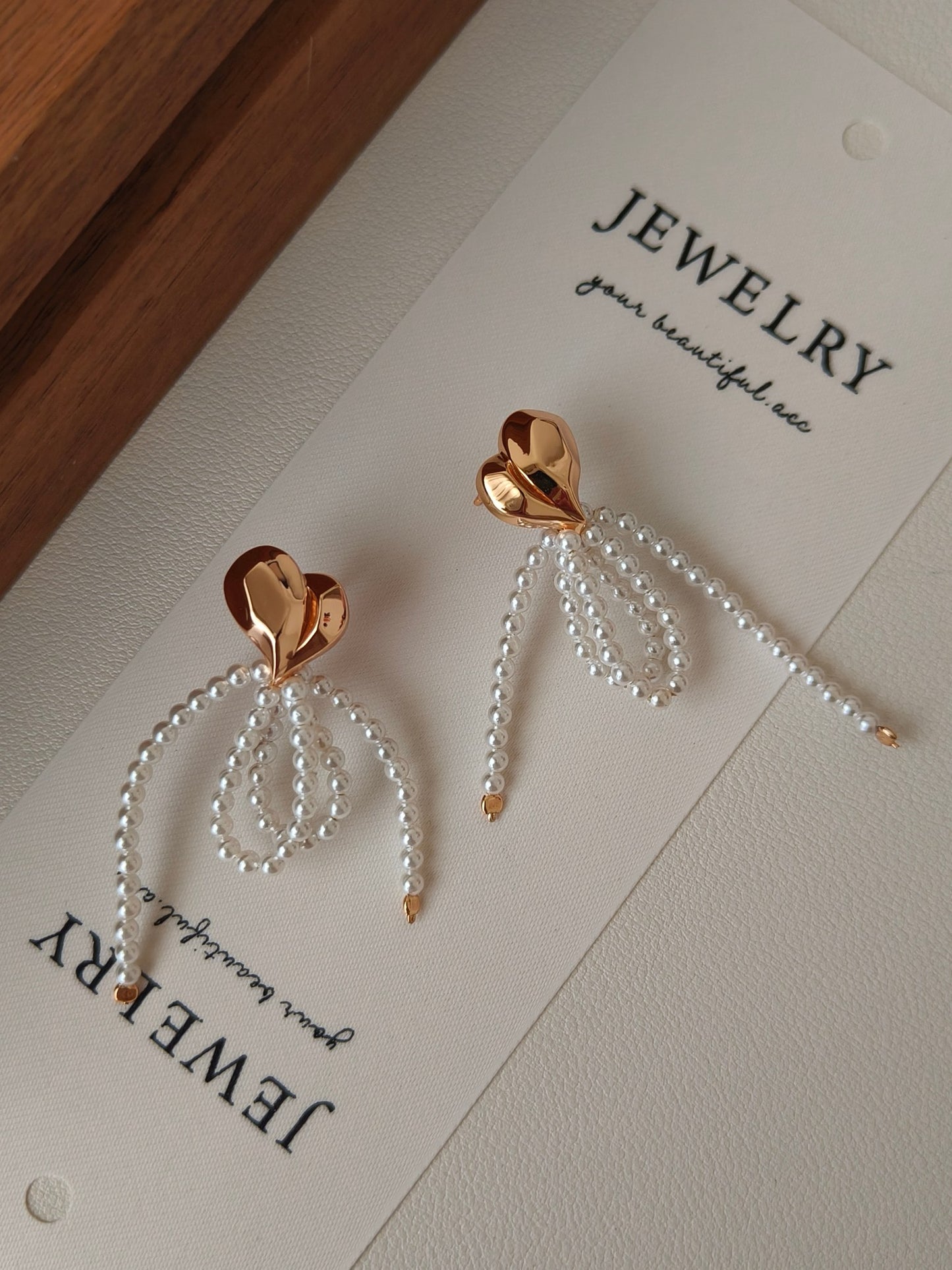 Heart-shaped earrings with pearl bow on a jewelry display card.