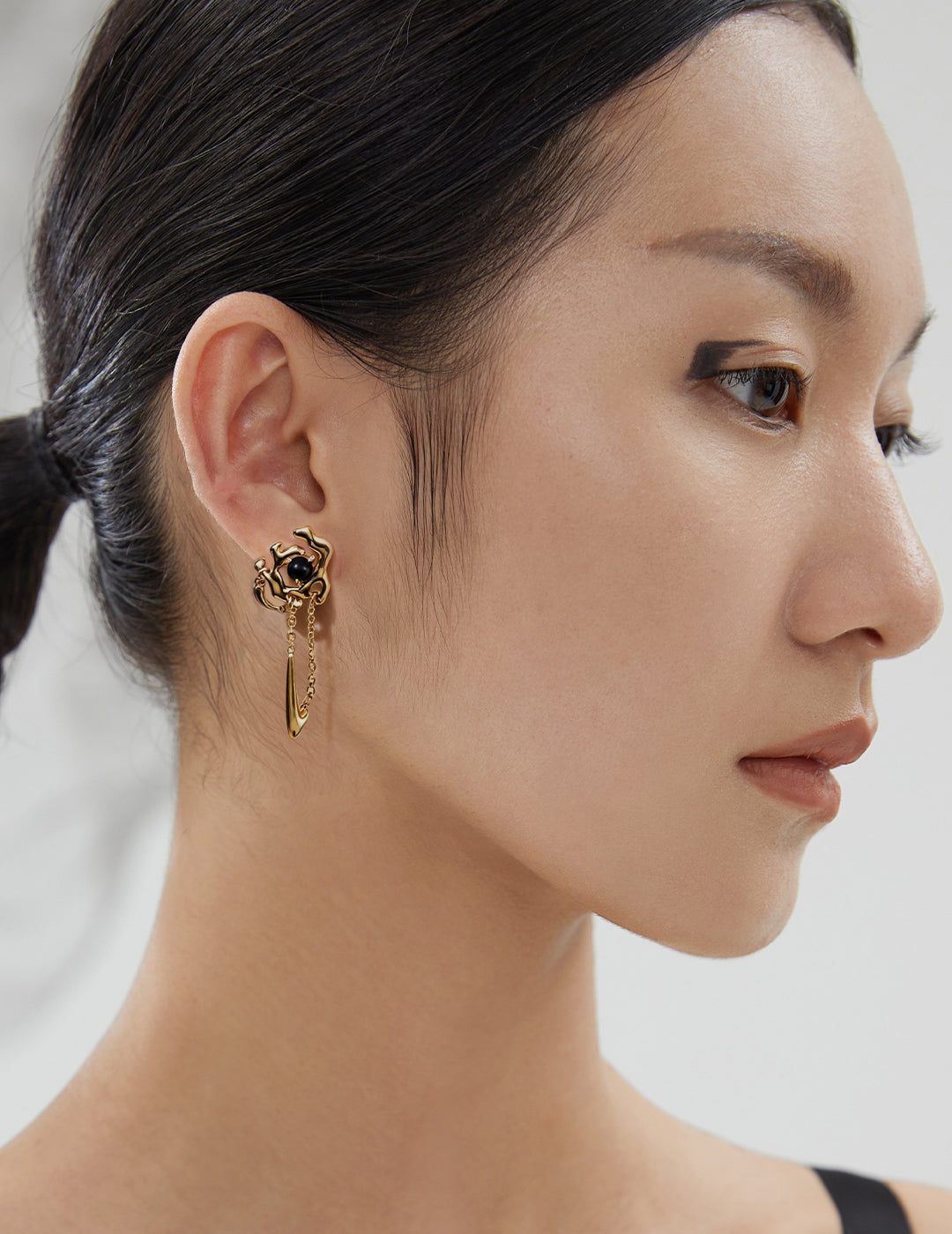 Close-up of a model wearing an ornate gold earring with a dark gemstone.