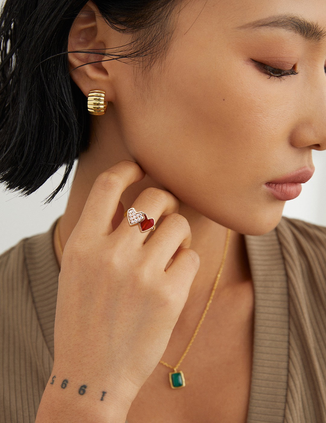 Close-up of a woman wearing red heart shaped gold ring with a neutral background.