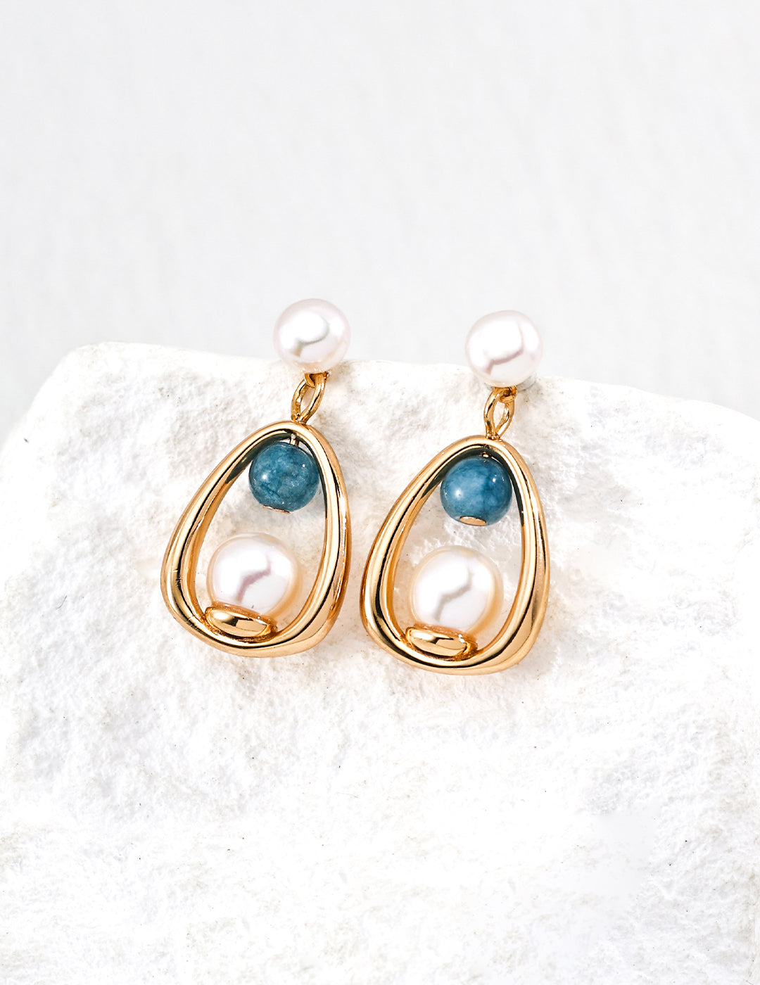 Pair of gold earrings with pearls and blue stones on a textured white surface