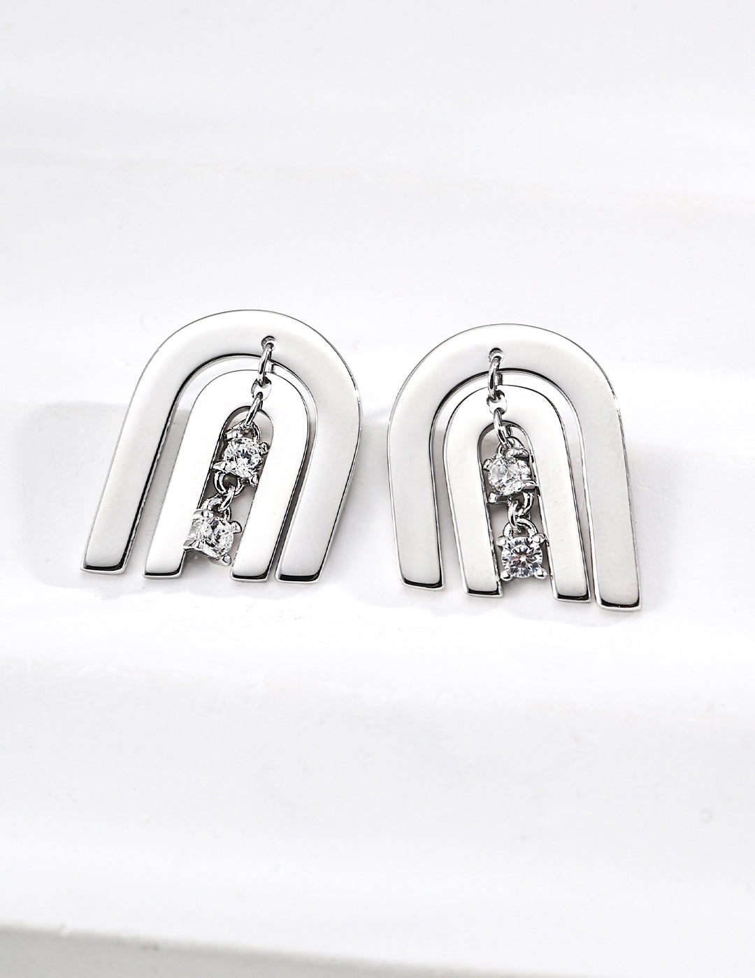 Contemporary CNC precision cut layered arch stud earrings with a central dangling cubic zirconia stone in silver finishes