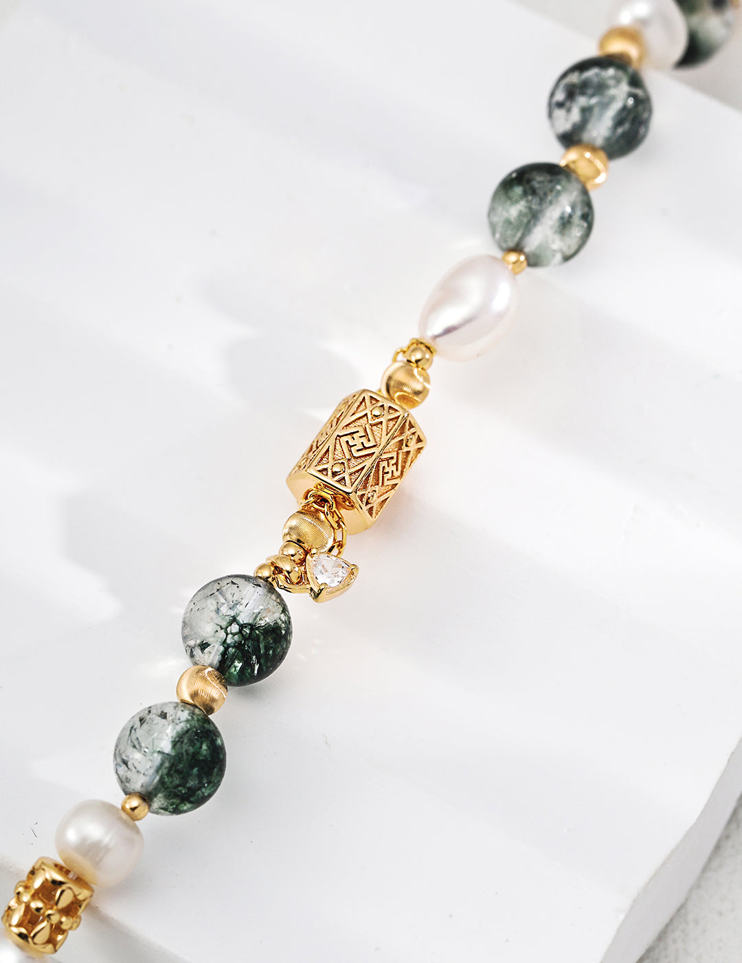 Beaded bracelet with green stones, pearls, and gold accents on a white surface