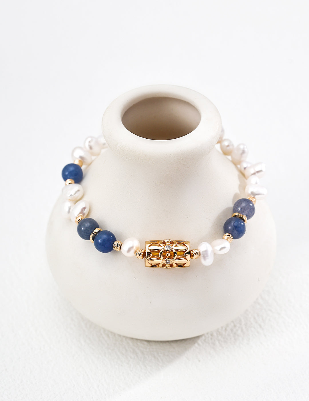 Bracelet with blue beads and gold accents on a white vase