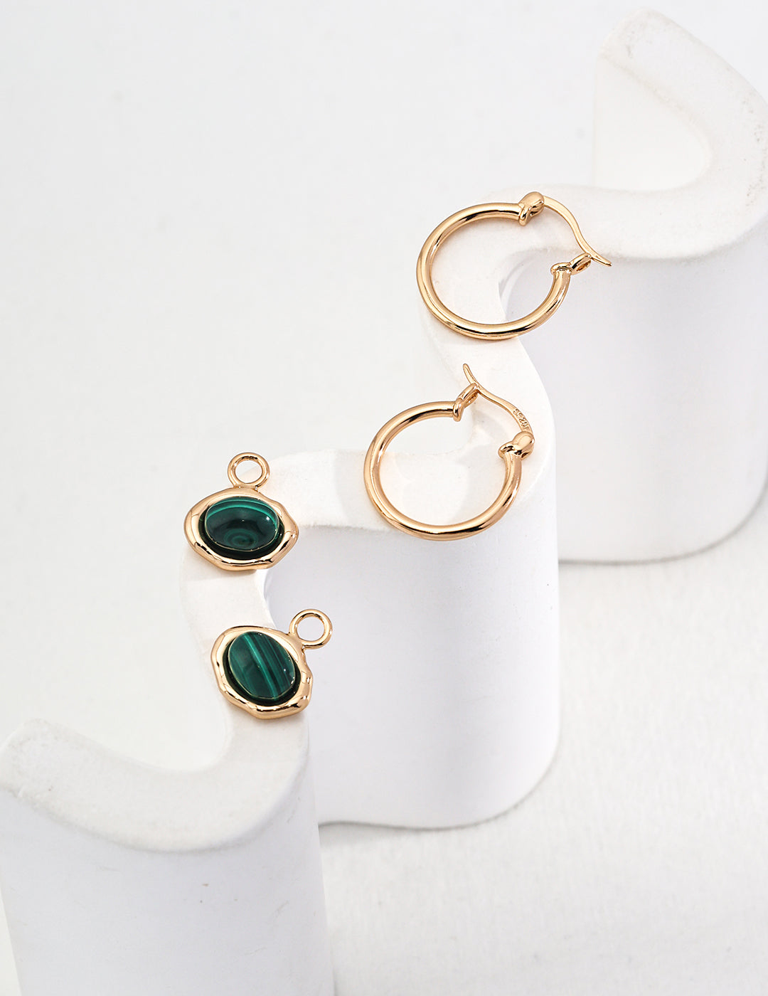 Gold hoop earrings with green gemstones on a white surface