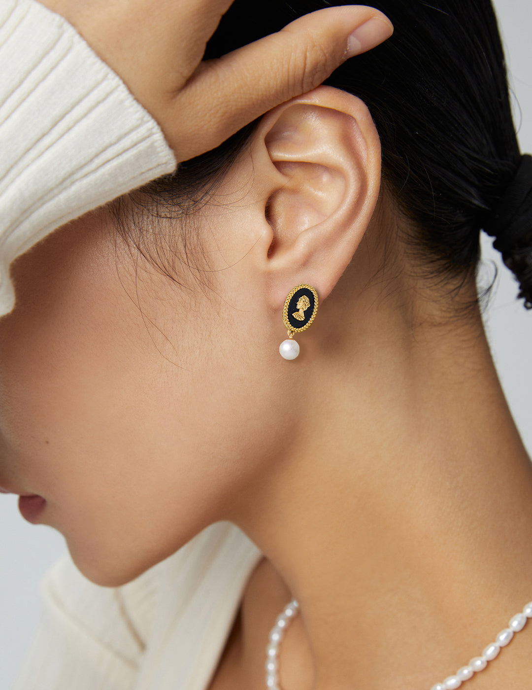 A model wearing vintage gold queen cameo drop earrings with premium black enamel backdrop and dangling natural freshwater pearls