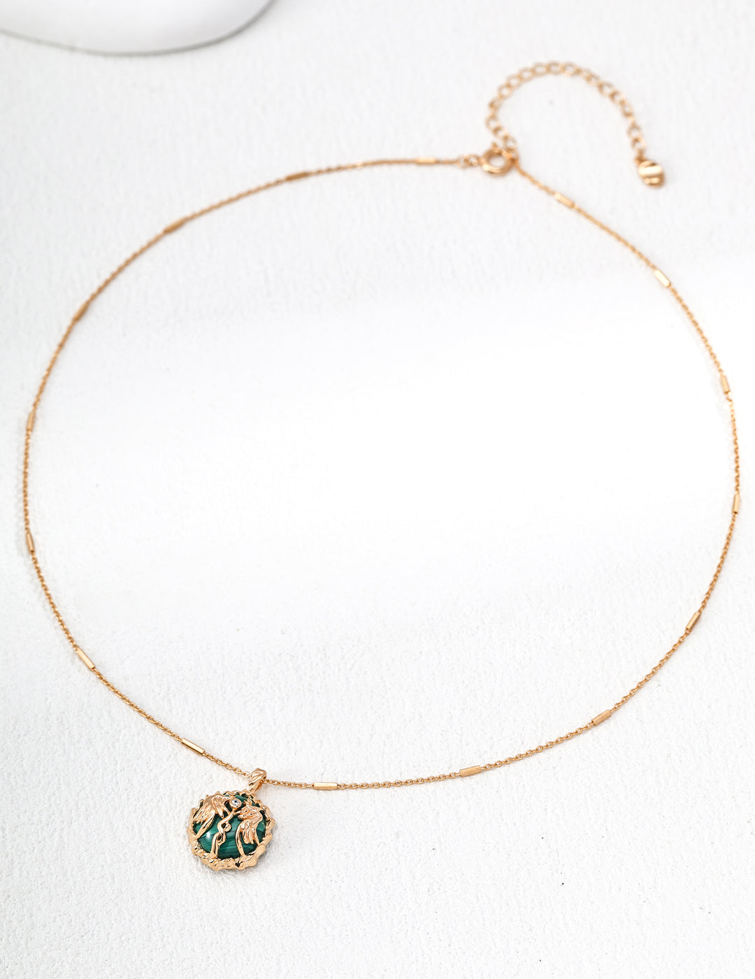 Gold necklace with a green pendant on a white background