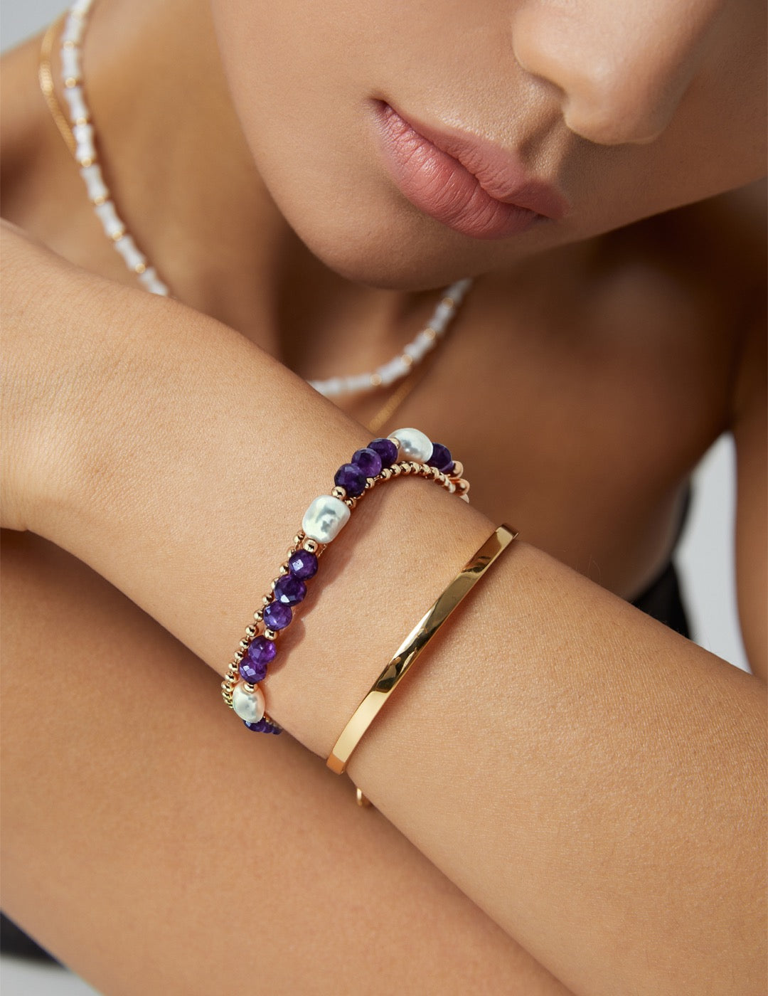 Close-up of a model wearing elegant double-strand bracelet with one layer of natural pearls and one layer of gold chain with purple amethyst gemstones