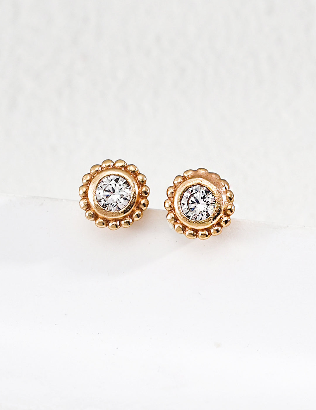 Pair of gold earrings with clear gemstones on a light background
