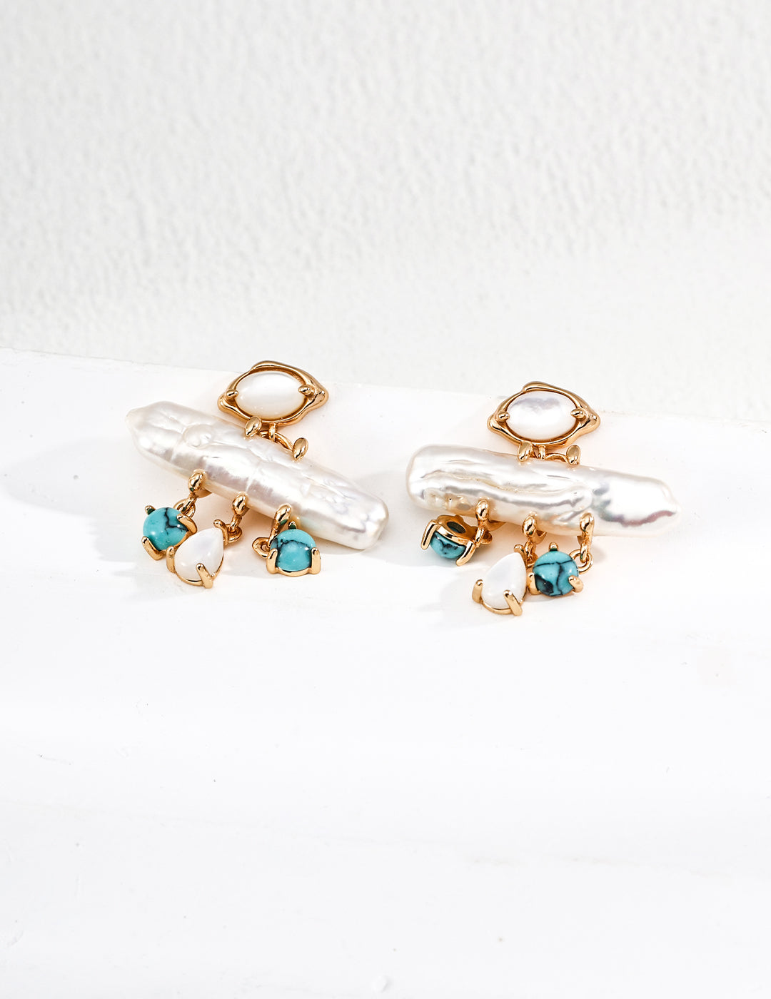 Pair of gold earrings with pearls and blue gemstones on a white background