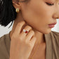Close-up of a woman wearing red heart shaped gold ring with a neutral background.