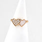 Heart-shaped ring with gold and white stones on a white stand