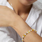 Close-up of a wrist wearing a bracelet with yellow and white beads, against a blurred background.