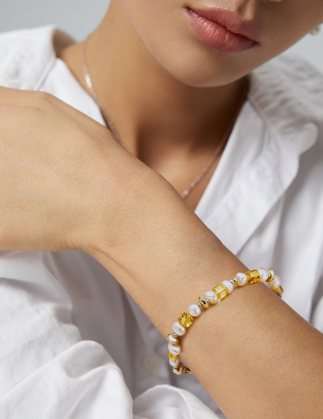 Close-up of a wrist wearing a bracelet with yellow and white beads, against a blurred background.