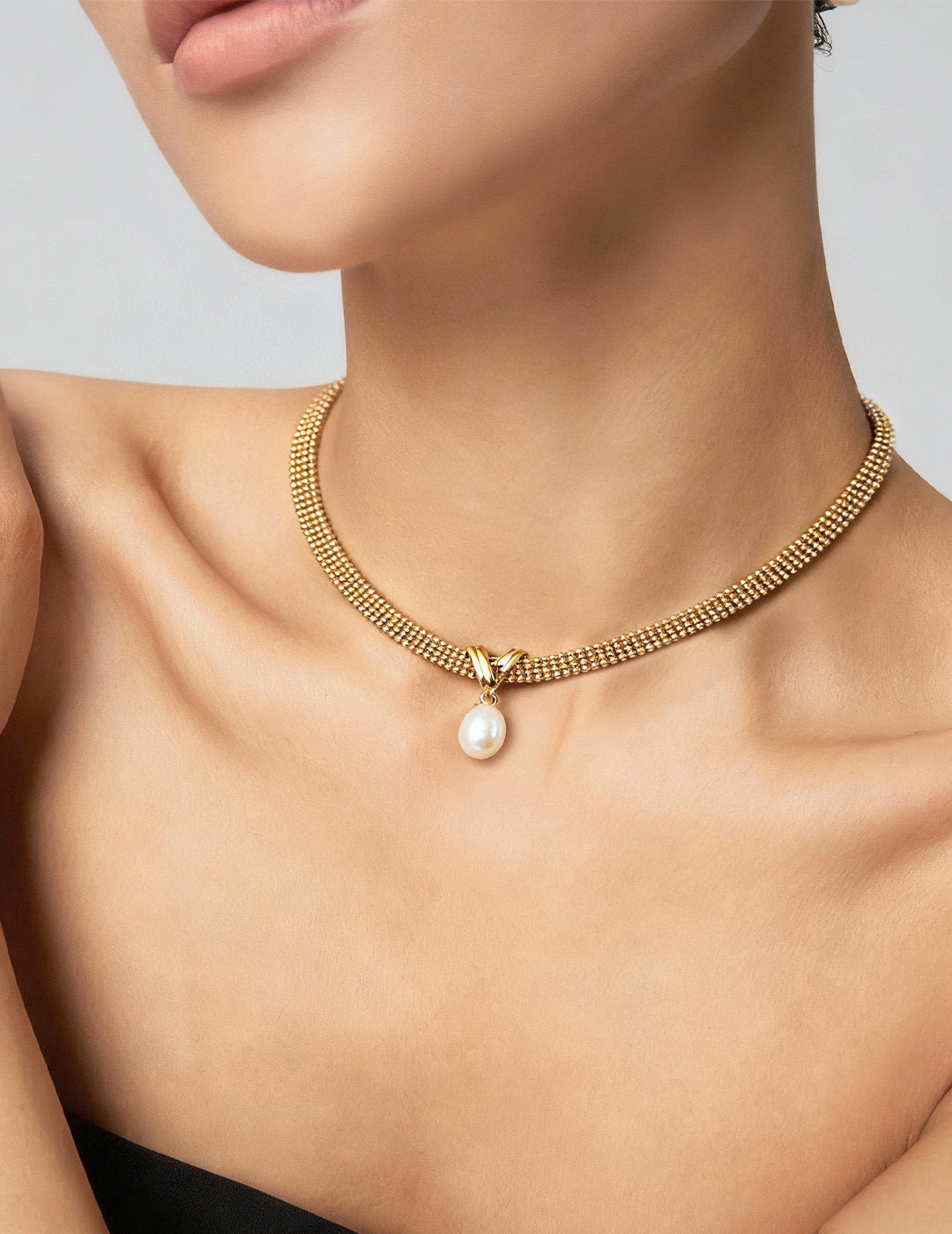 Gold necklace with a pearl pendant on a model against a neutral background