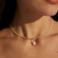Close-up of a woman wearing a gold necklace with a pearl pendant.