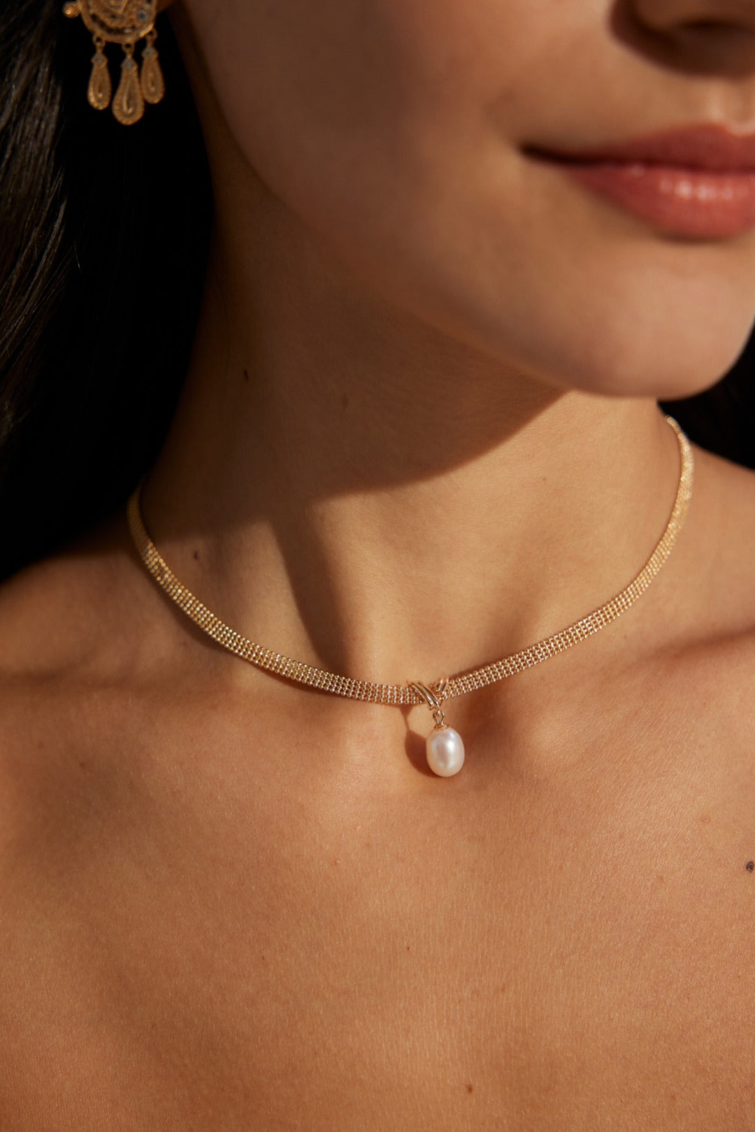 Close-up of a woman wearing a gold necklace with a pearl pendant.