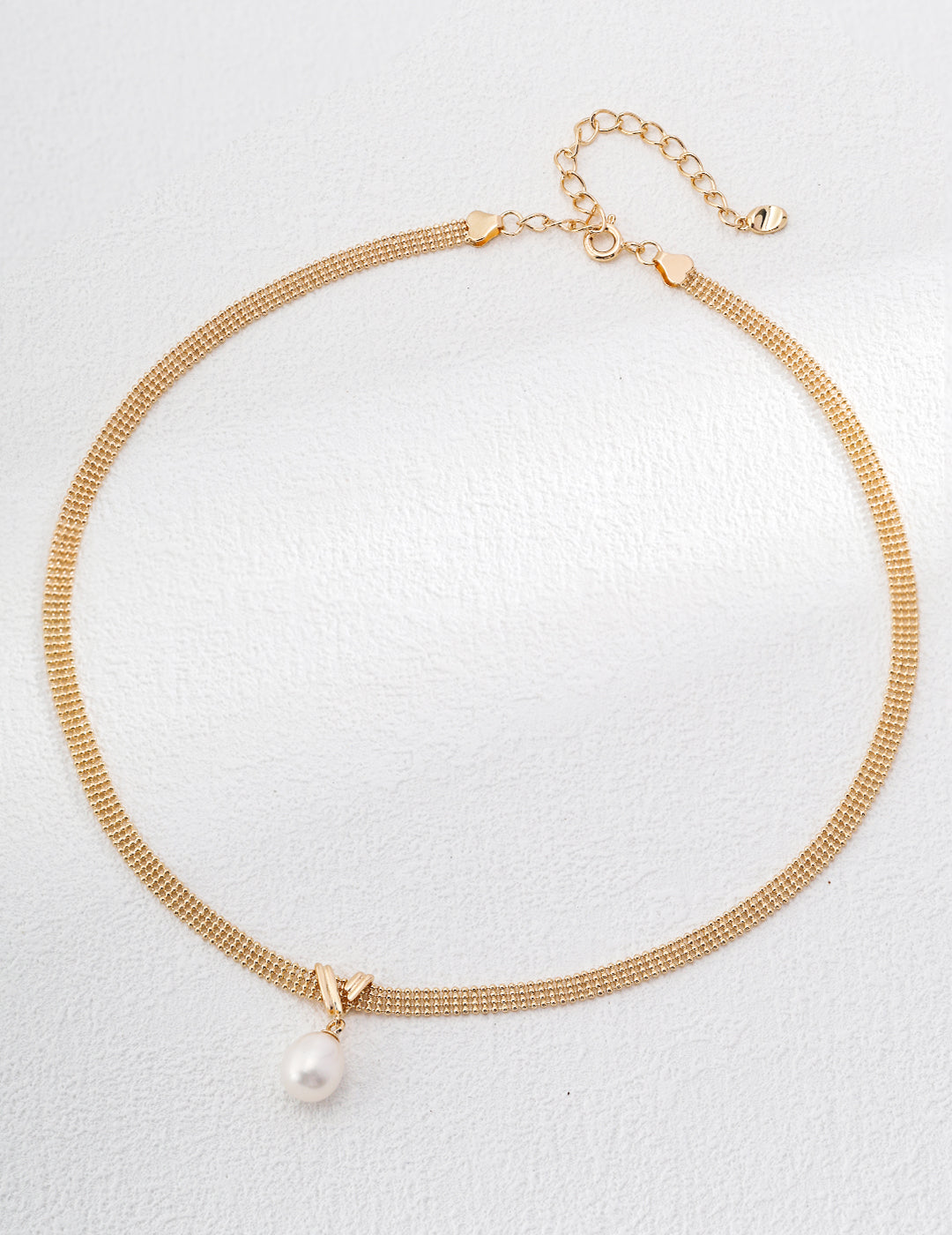 Gold necklace with a pearl pendant on a light gray background