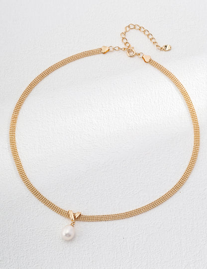 Gold necklace with a pearl pendant on a light gray background