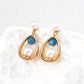 Pair of gold earrings with pearls and blue stones on a textured white surface