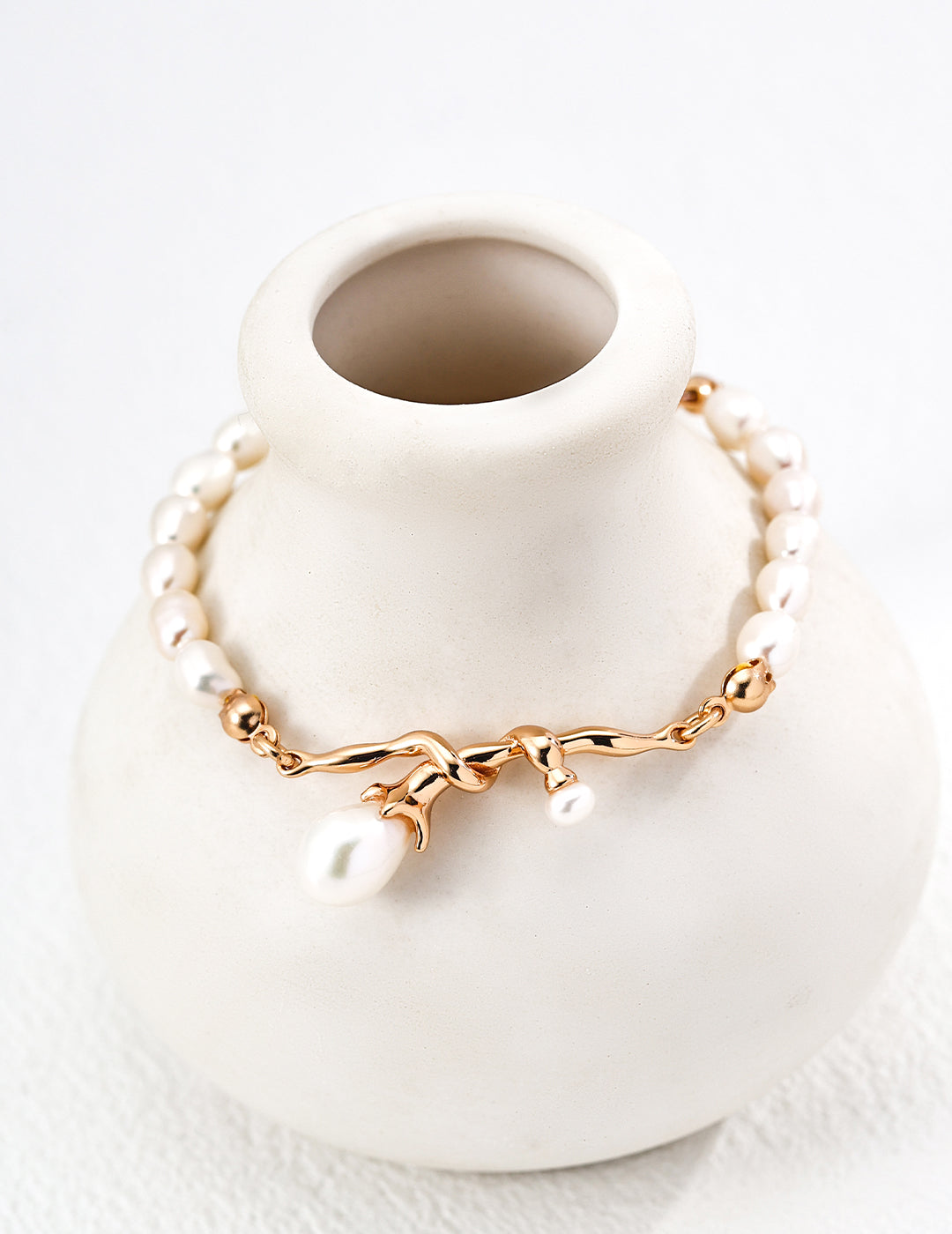 Close-up look of the elegant retro gold bracelet with a central fluid intertwined vine knot holding natural freshwater pearl charms on a lustrous pearl strand