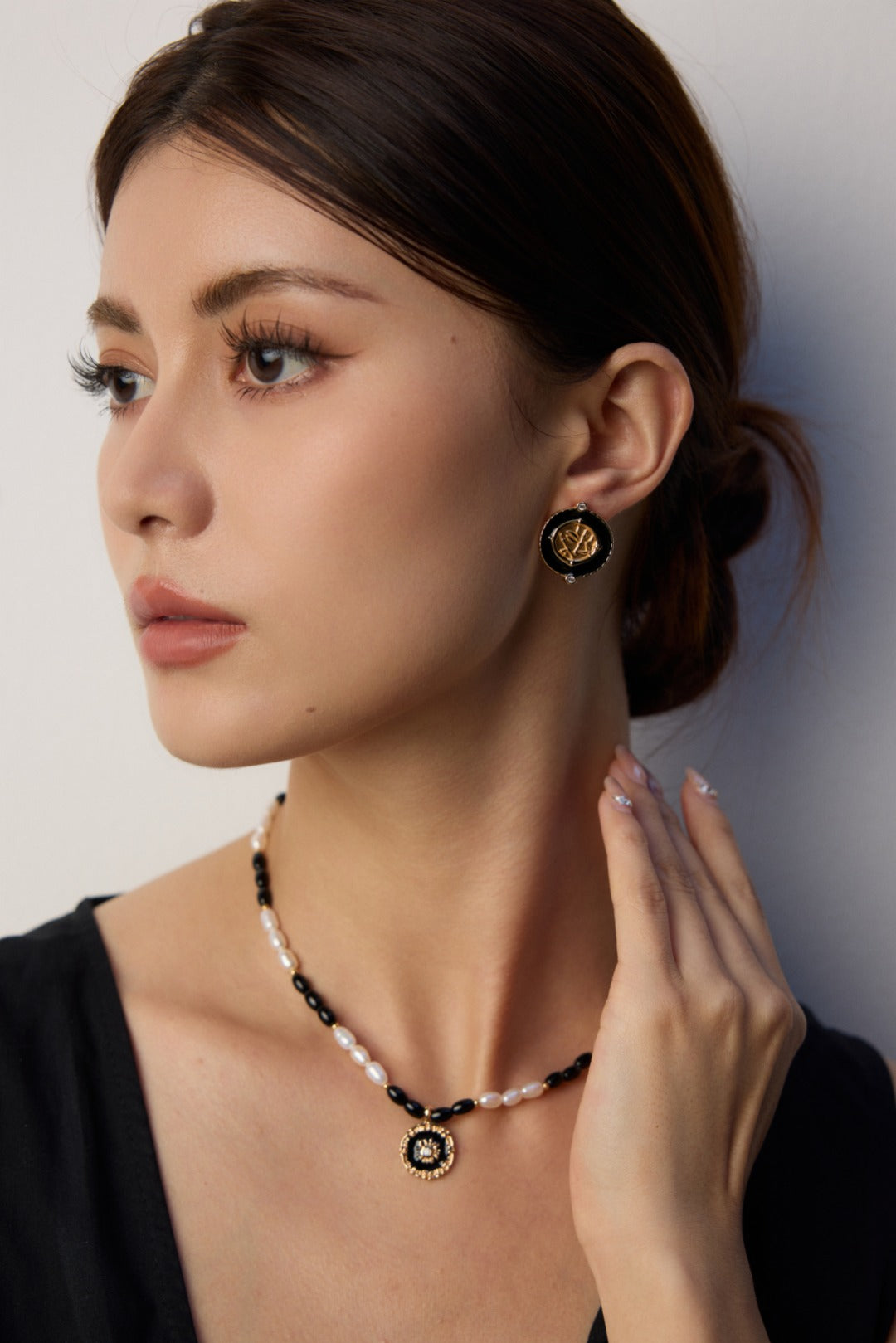 A model wearing a chinoiserie chic round stud earrings with black enamel borders centering a metallic bamboo relief plaque with micro cz gems in gold