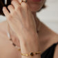 Close-up of a person wearing a sleek 18k gold plated flat herringbone snake chain bracelets with a central bezel-set oval natural tiger's eye stone