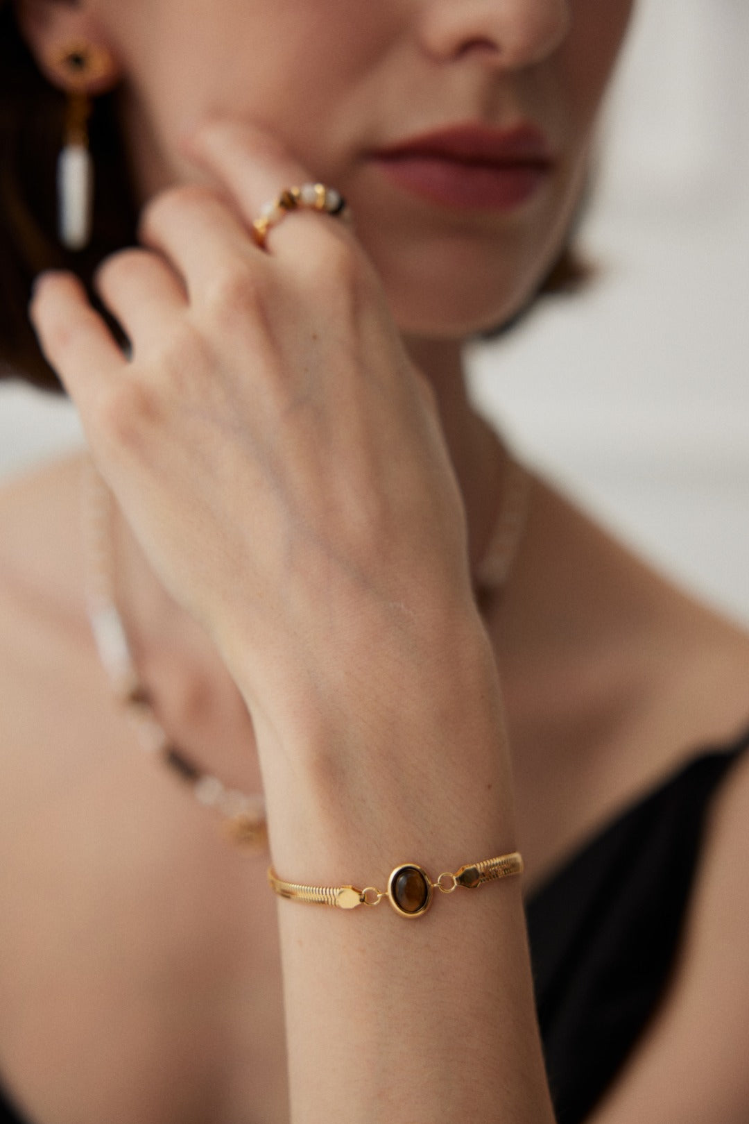 Close-up of a person wearing a sleek 18k gold plated flat herringbone snake chain bracelets with a central bezel-set oval natural tiger's eye stone