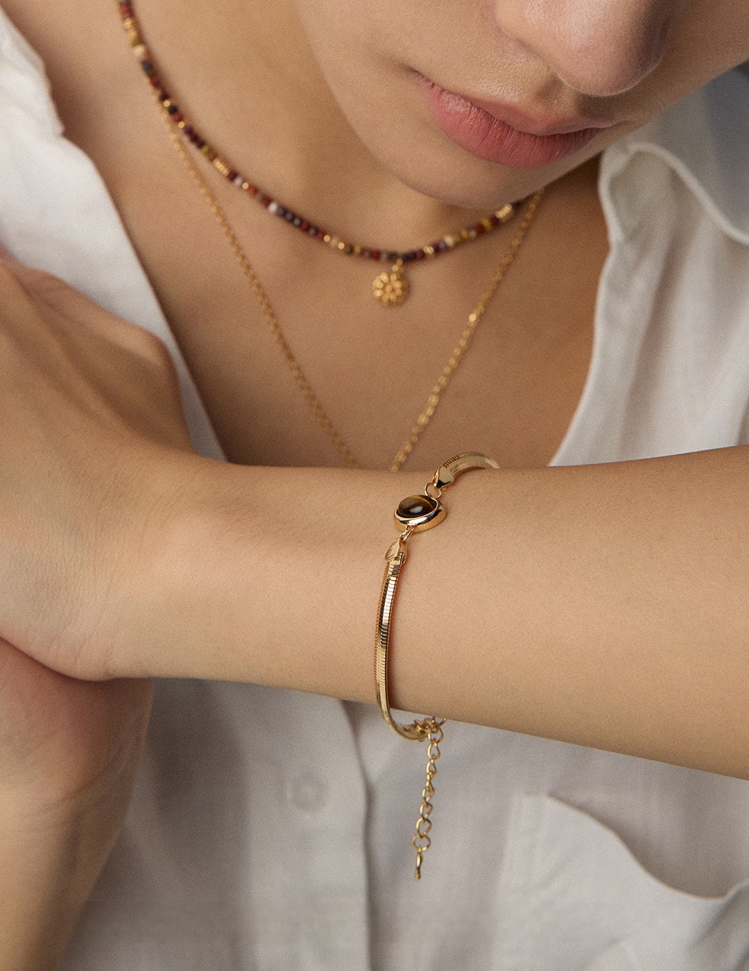 A model wearing a sleek 18k gold plated flat herringbone snake chain bracelets with a central bezel-set oval natural tiger's eye stone