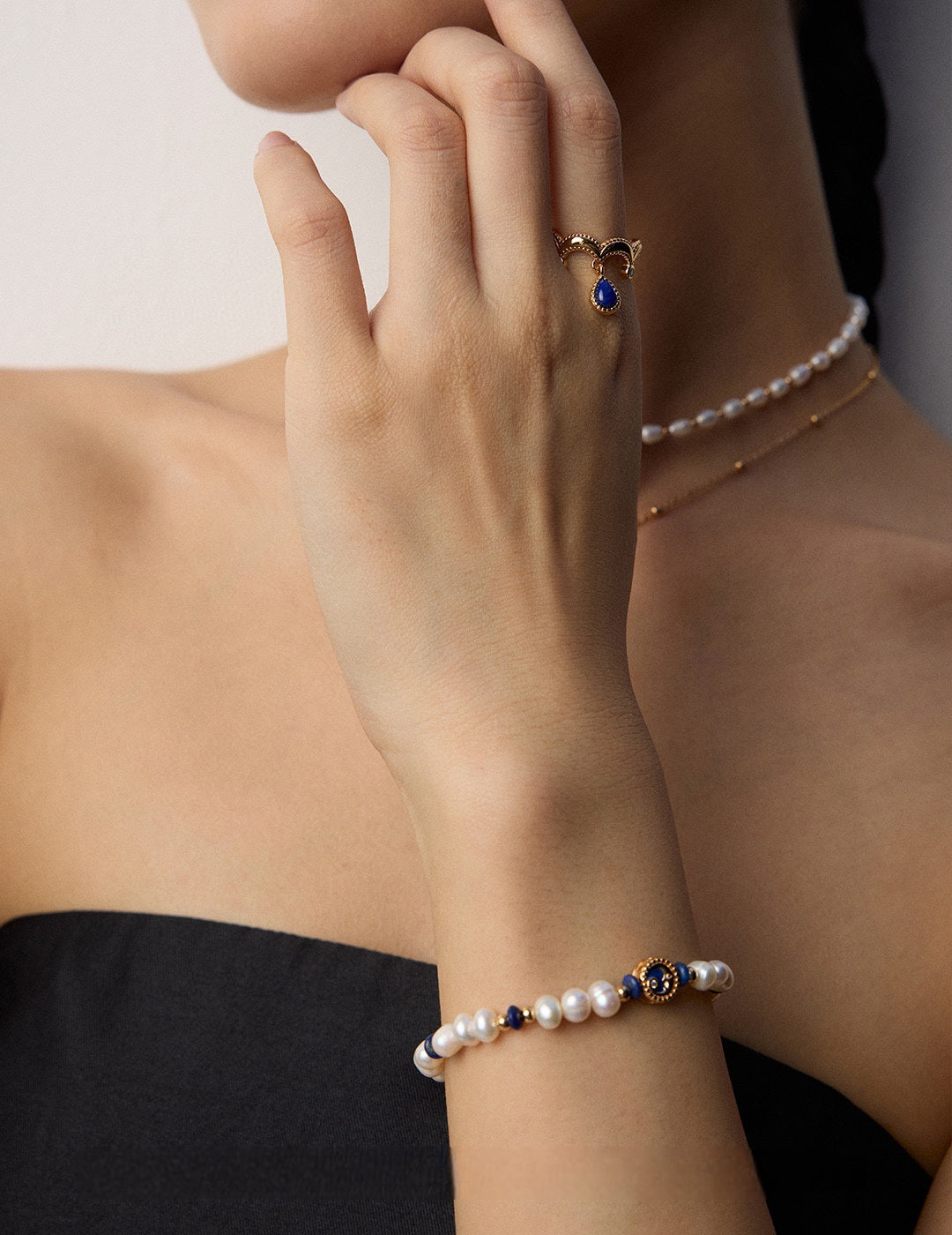 Close-up of a model wearing a luminous natural freshwater pearl strand bracelet with dark blue lapis lazuli accents and a central gold celestial crescent moon charm with a cz crystal