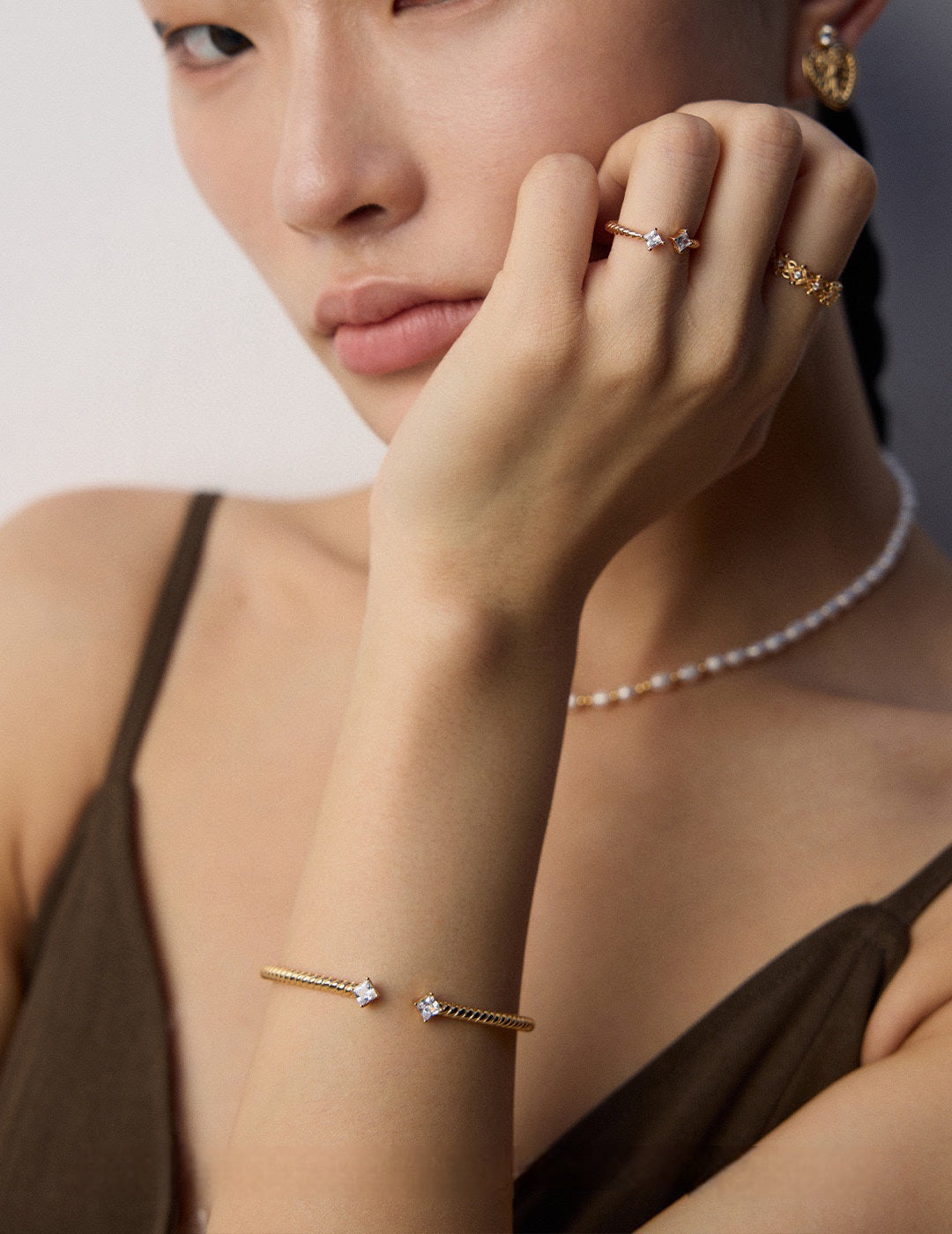 A model wearing contemporary minimalist open-band cuff bracelet and matching ring set in gold finishes featuring radiant prong-set cz gems flanking both open ends