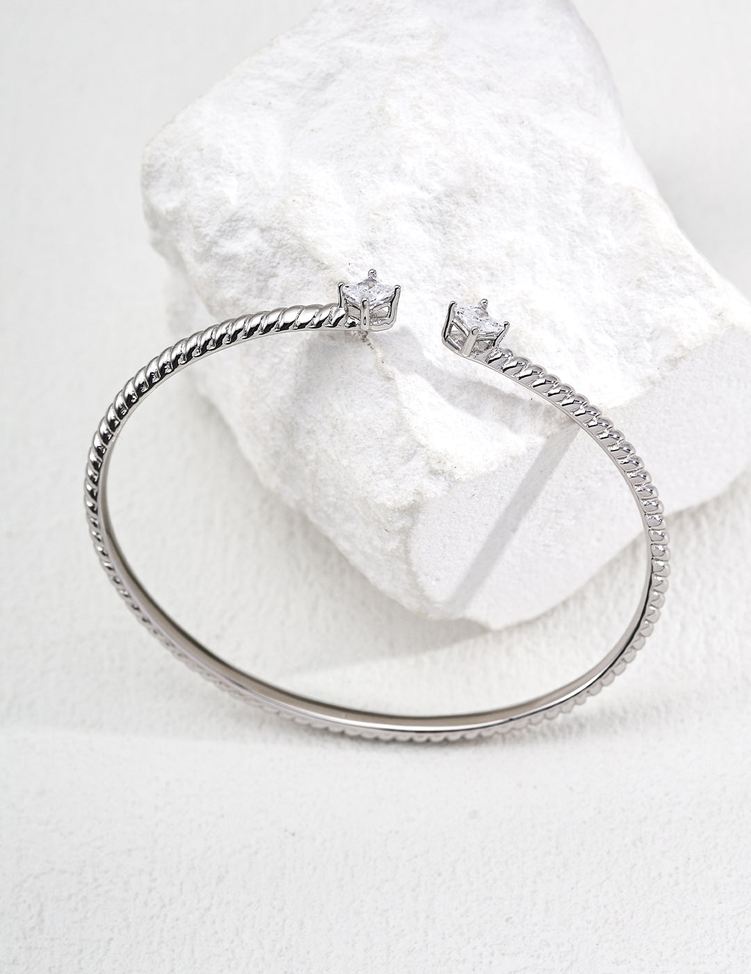 Contemporary minimalist open-band cuff bracelet in silver finishes featuring radiant prong-set cz gems flanking both open ends
