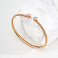Contemporary minimalist open-band cuff bracelet in gold finishes featuring radiant prong-set cz gems flanking both open ends