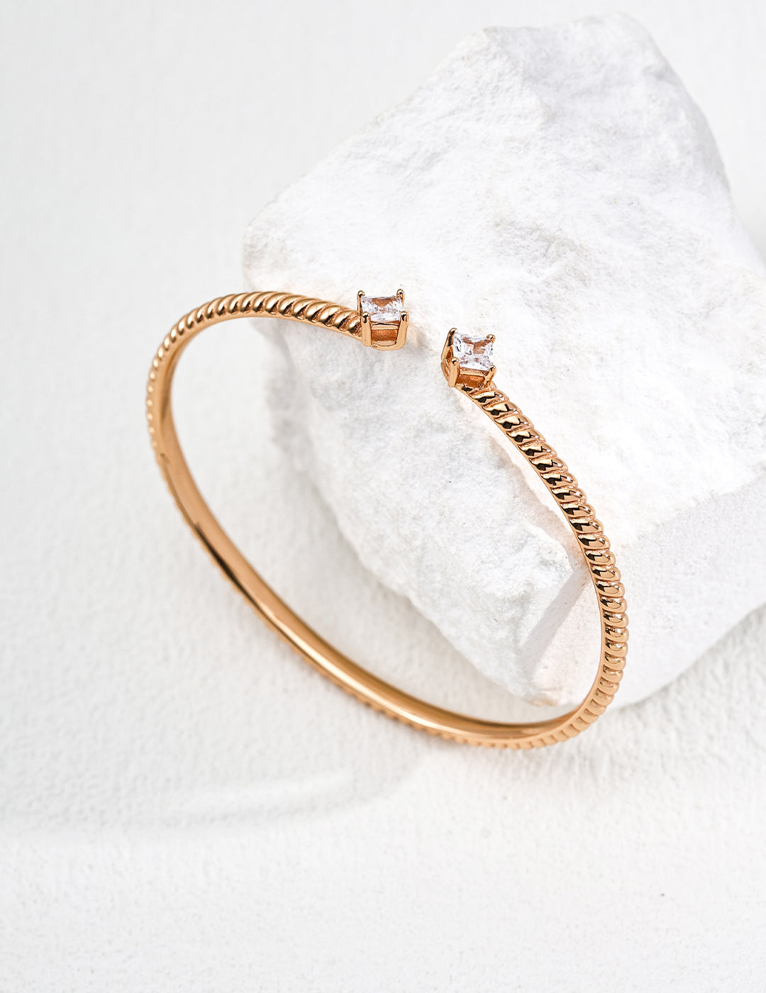 Contemporary minimalist open-band cuff bracelet in gold finishes featuring radiant prong-set cz gems flanking both open ends
