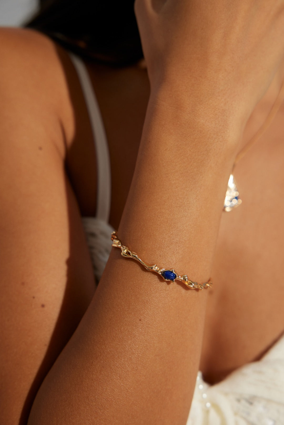 A model wearing an antique style statement open cuff bracelet featuring an organic fluid molten gold texture centering a smooth oval natural blue lapis lazuli stone