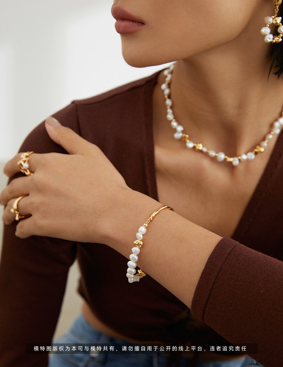 Close-up of a person wearing gold jewelry with pearls on a neutral background