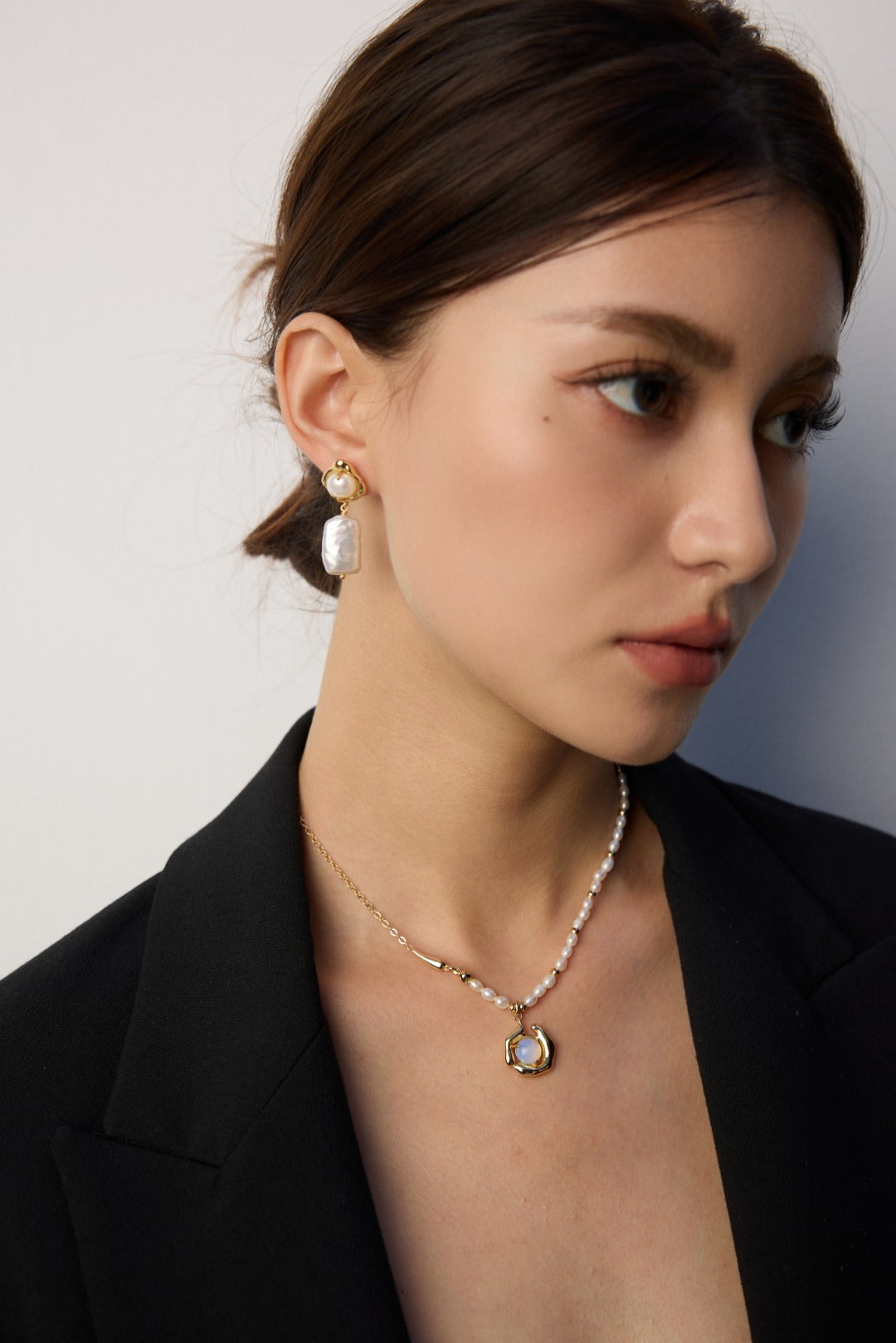 Woman wearing a necklace and earrings against a neutral background