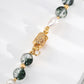 Beaded bracelet with green stones, pearls, and gold accents on a white surface