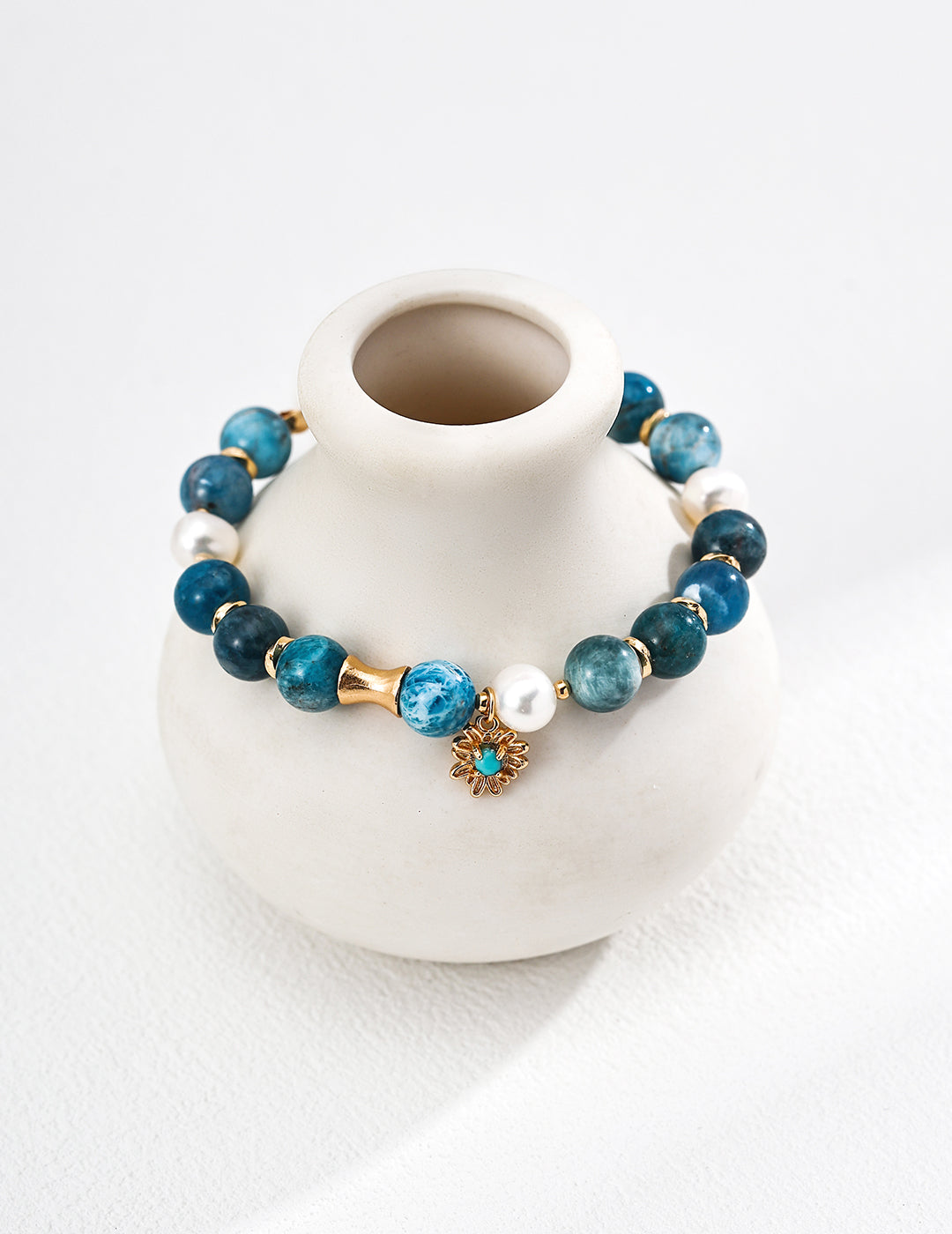 Blue beaded bracelet with gold accents on a white vase against a white background