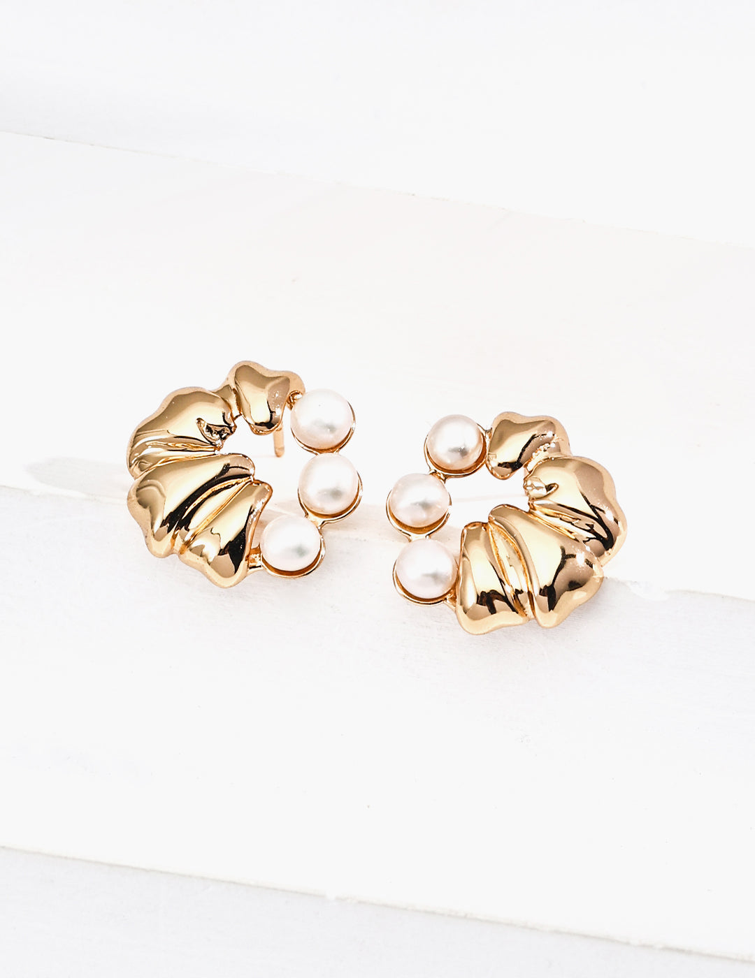 Gold earrings with pearl accents on a white background
