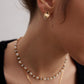 A model wearing an avant-garde geometric stud earrings featuring fine deconstructive metallic wire loops and two staggered floating white shell pearls in gold