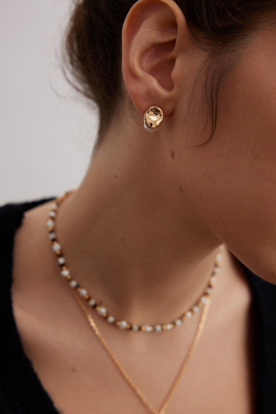 A model wearing an avant-garde geometric stud earrings featuring fine deconstructive metallic wire loops and two staggered floating white shell pearls in gold