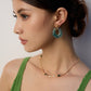 A model wearing art-gallery style drop earrings featuring smoky translucent ink-green moss agate faux resin hoops held by a geometric 18k gold plated claw with pavé cz crystals