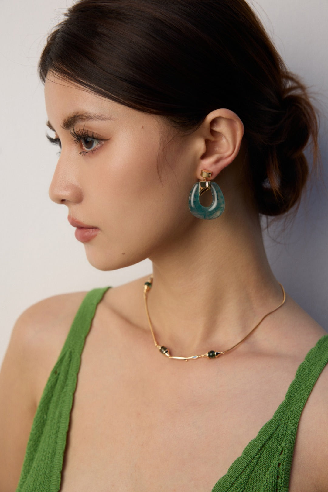A model wearing art-gallery style drop earrings featuring smoky translucent ink-green moss agate faux resin hoops held by a geometric 18k gold plated claw with pavé cz crystals