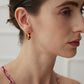 A model wearing avant-garde geometric heart stud earrings featuring asymmetrical cutout fluid metallic loops with high-polished black and white enamel inlay