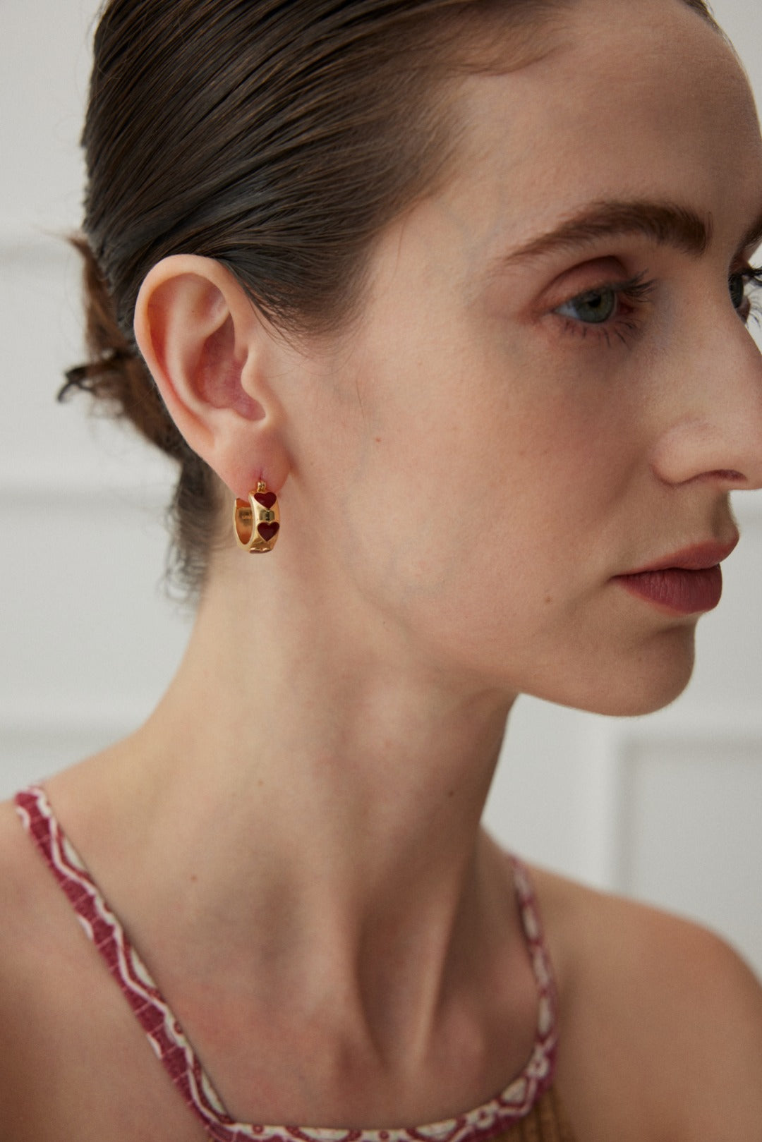 A model wearing avant-garde geometric heart stud earrings featuring asymmetrical cutout fluid metallic loops with high-polished black and white enamel inlay