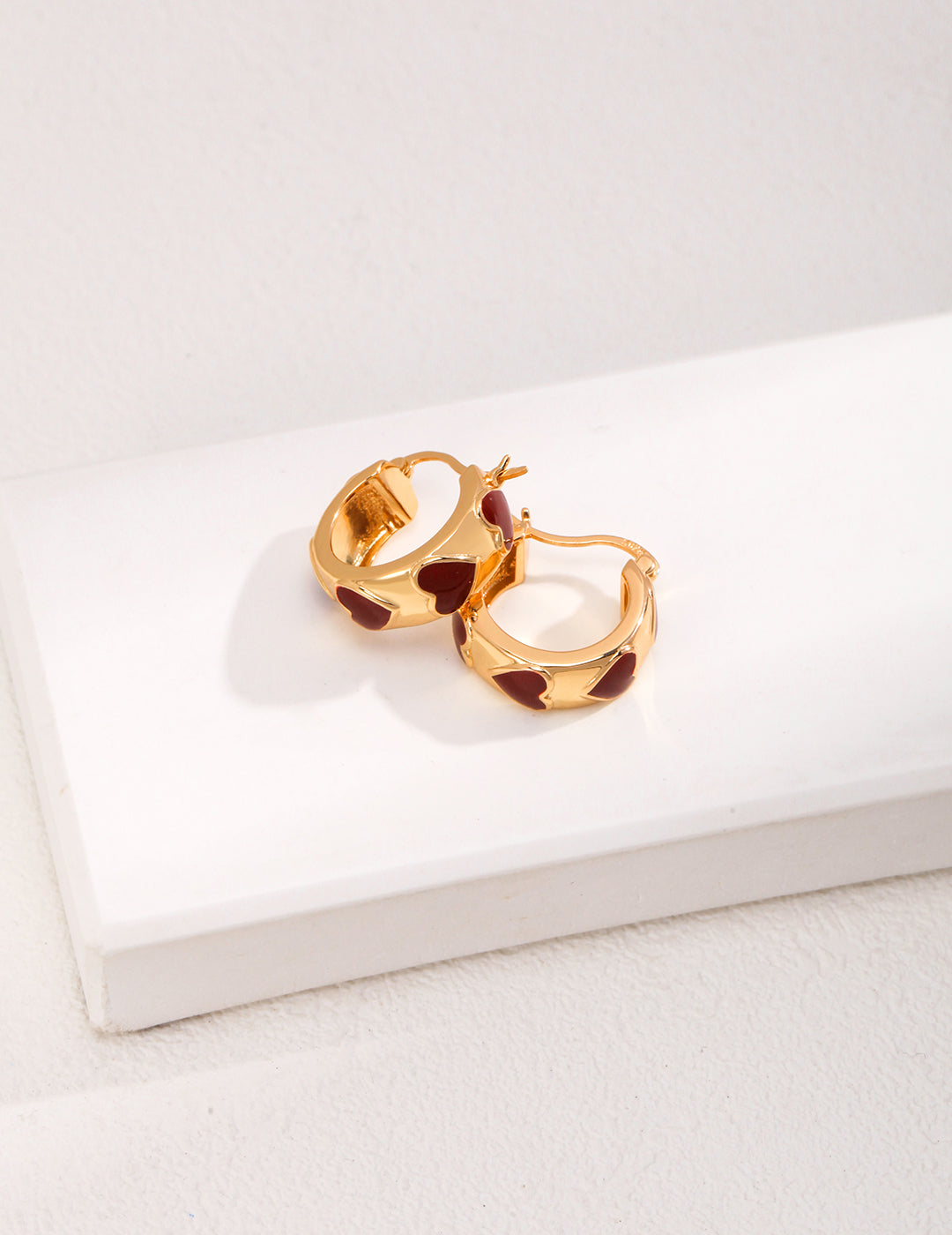 Gold hoop earrings with red hearts on a white surface