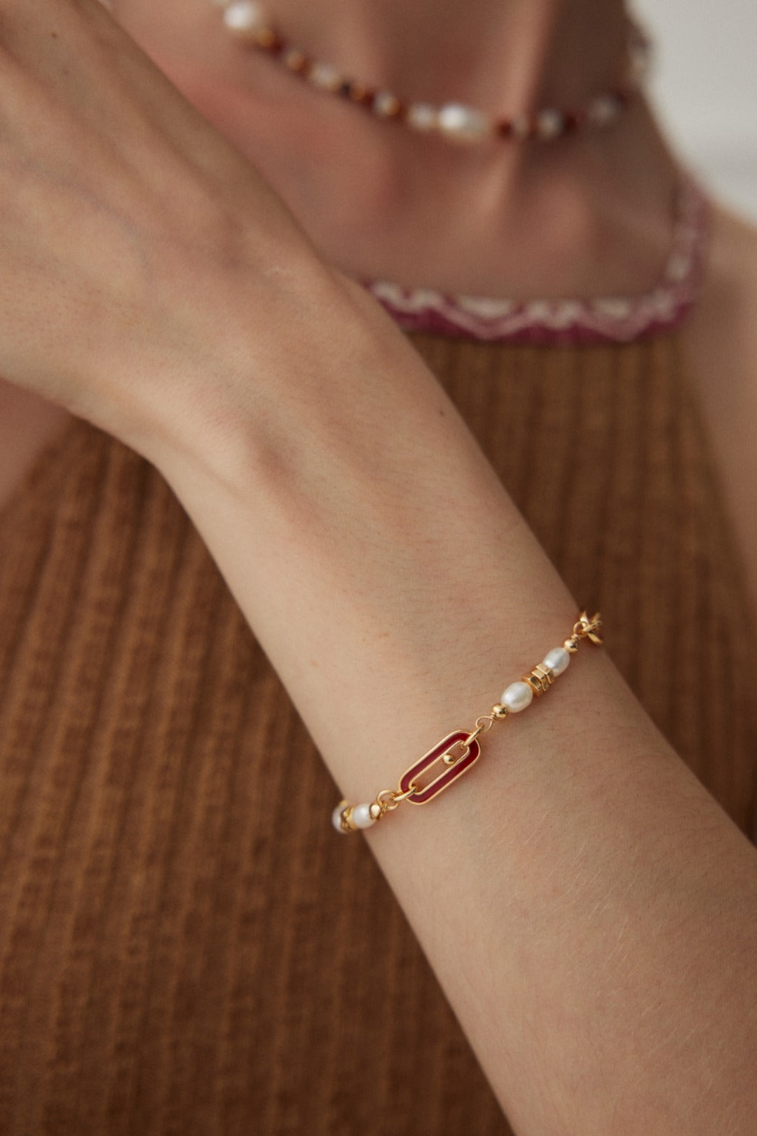 A model wearing a luxury 18k gold plated bracelet featuring rice freshwater pearls, crimson red enamel oblong links, and an adjustable chain slider closure