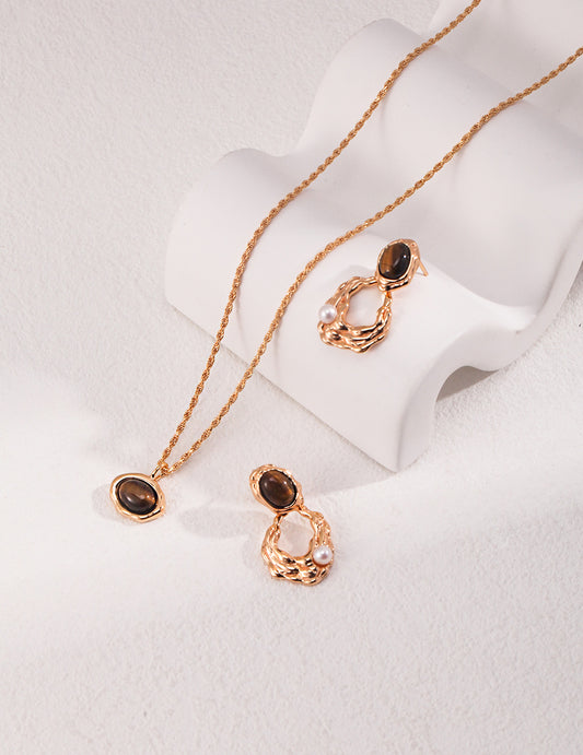 Dare To Sparkle - Luxury resort jewelry set displaying an organic molten gold framed round tiger's eye pendant necklace and matching tiger's eye earrings with delicate floating pearl drops