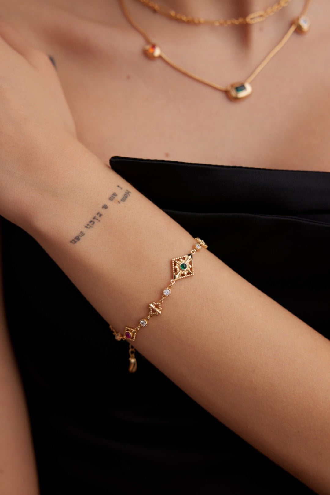 Gold bracelet with gemstones on a wrist against a black background