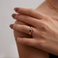 Close-up of a hand wearing a gold ring with a green gemstone on a neutral background